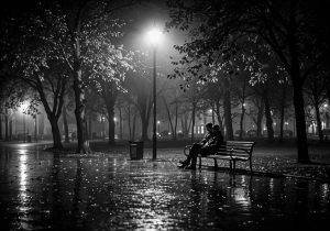 Schwarz-Weiß-Fotografie: Zwei Menschen sitzen allein auf einer Parkbank unter einer Laterne im nächtlichen Regen – Armin Mumper.
