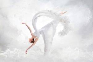 Eine Ballettänzerin in weißem Kleid vor weißem wolkigen Rauch tanzt eine Figur stehend auf einen Bein den Körper nach unten geneigt.